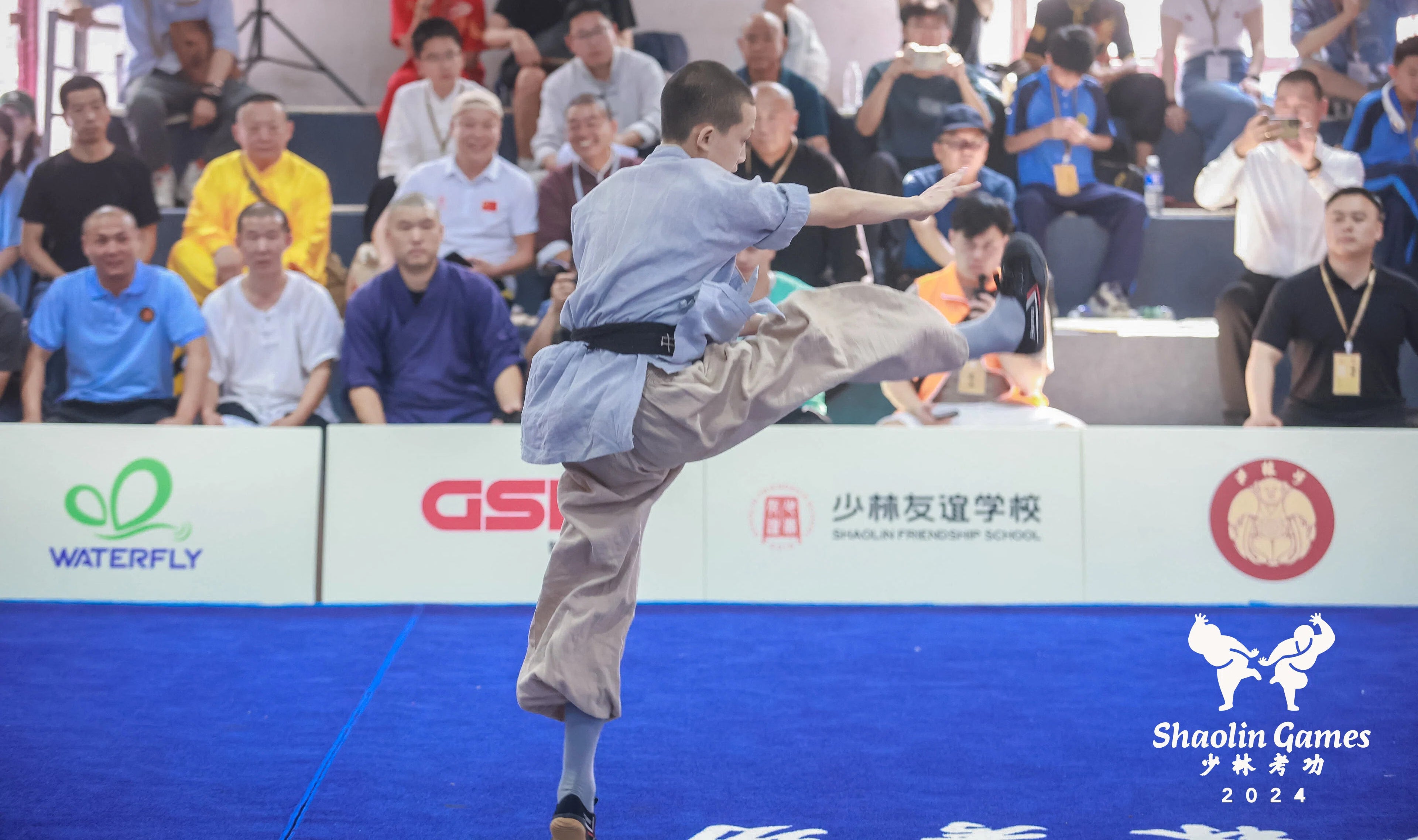 A young martial artist performing at the Shaolin Kung Fu Games 2024, with WATERFLY branding beside the event arena